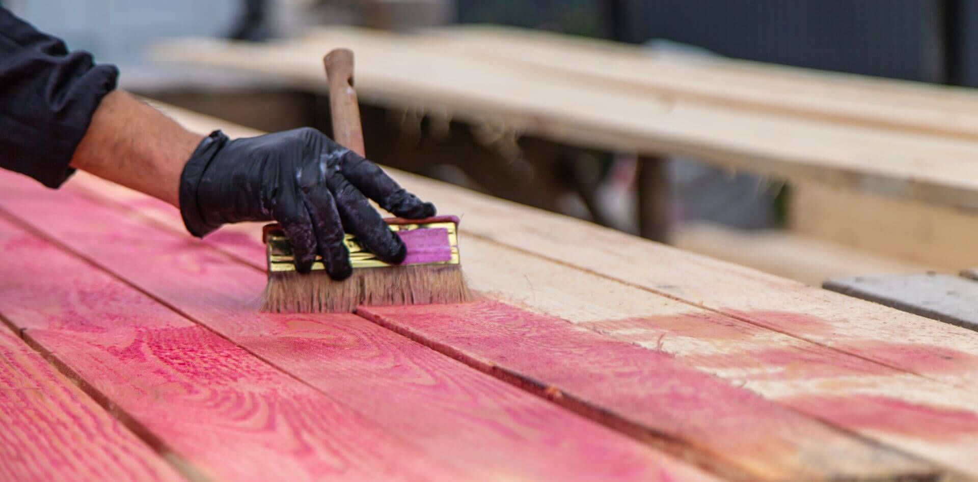 A person is staining a wooden deck with a brush.