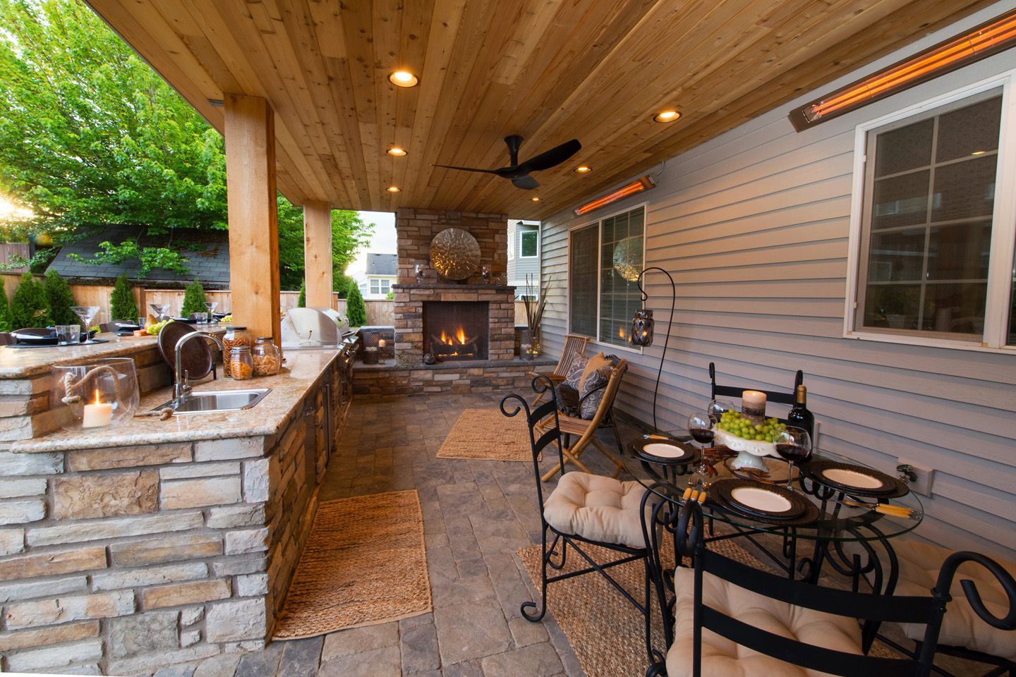 Spacious outdoor kitchen and fireplace under a deck, featuring stainless steel appliances
