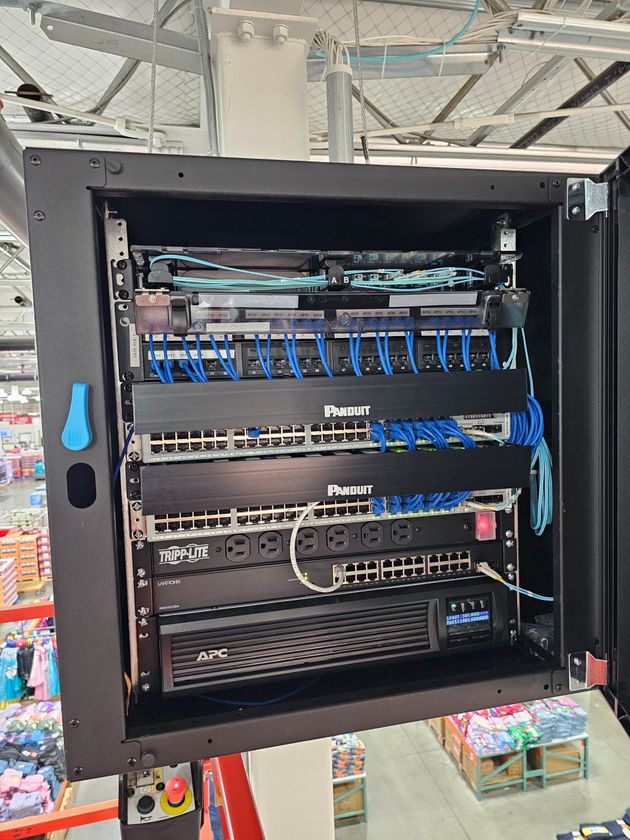 A black wall-mounted server rack holding network equipment, cabling, and an APC uninterruptible power supply.