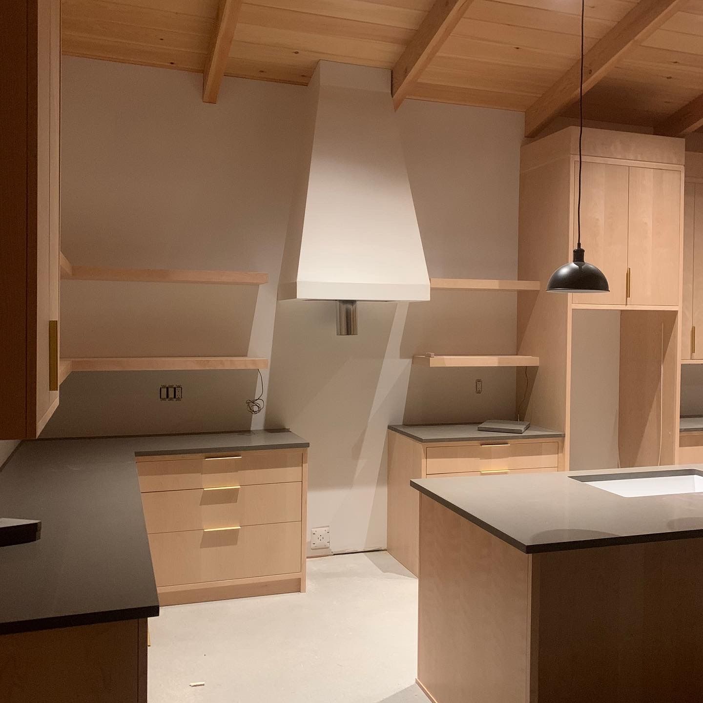 Kitchen with light wood cabinets, gray countertops, and a white range hood.