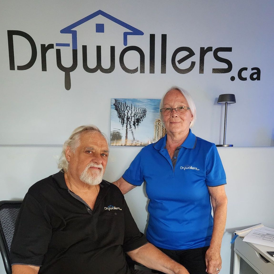 A man and a woman standing in front of a drywallers.ca sign