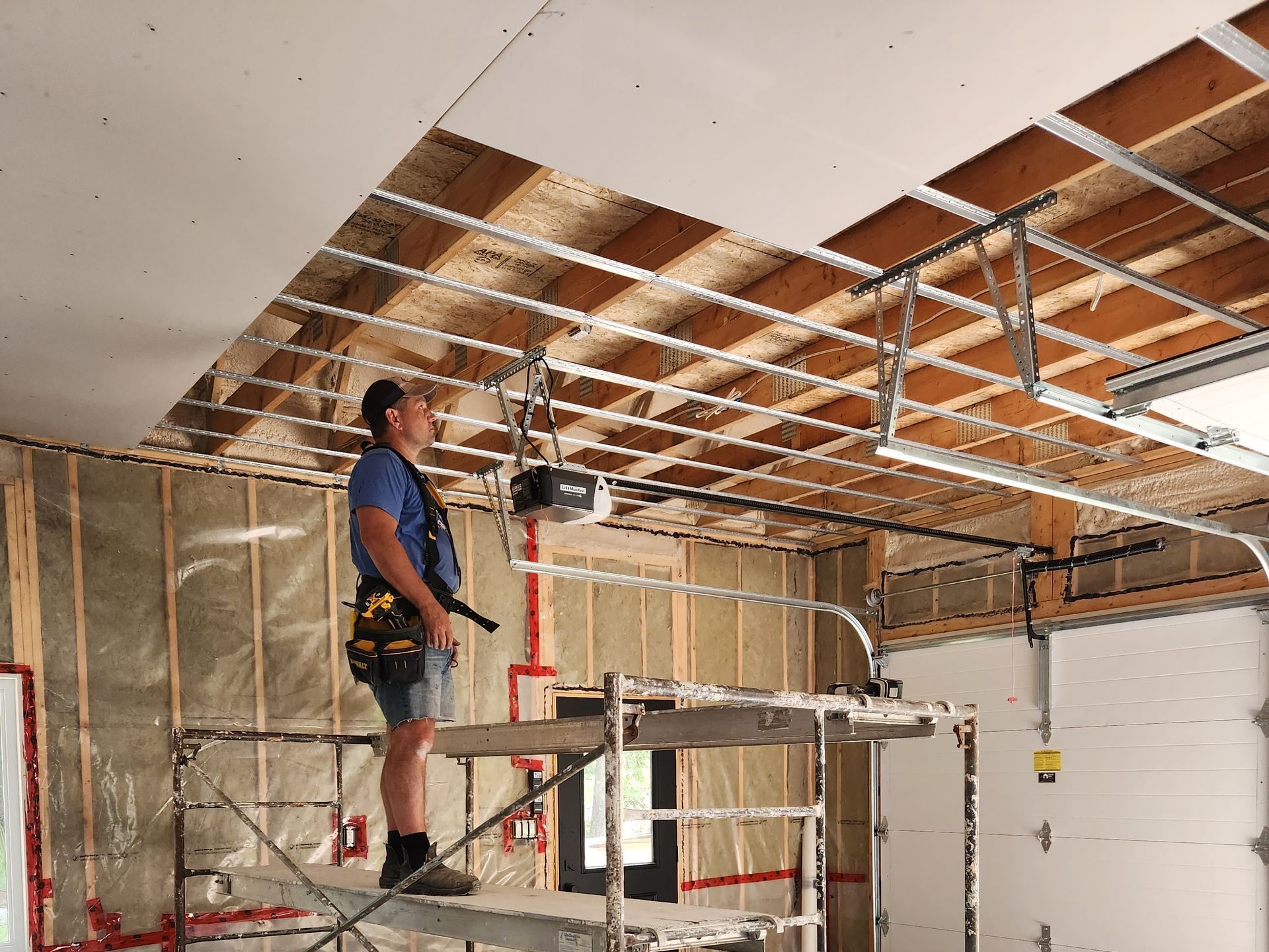 A man is standing on a scaffolding in a garage looking at the ceiling.