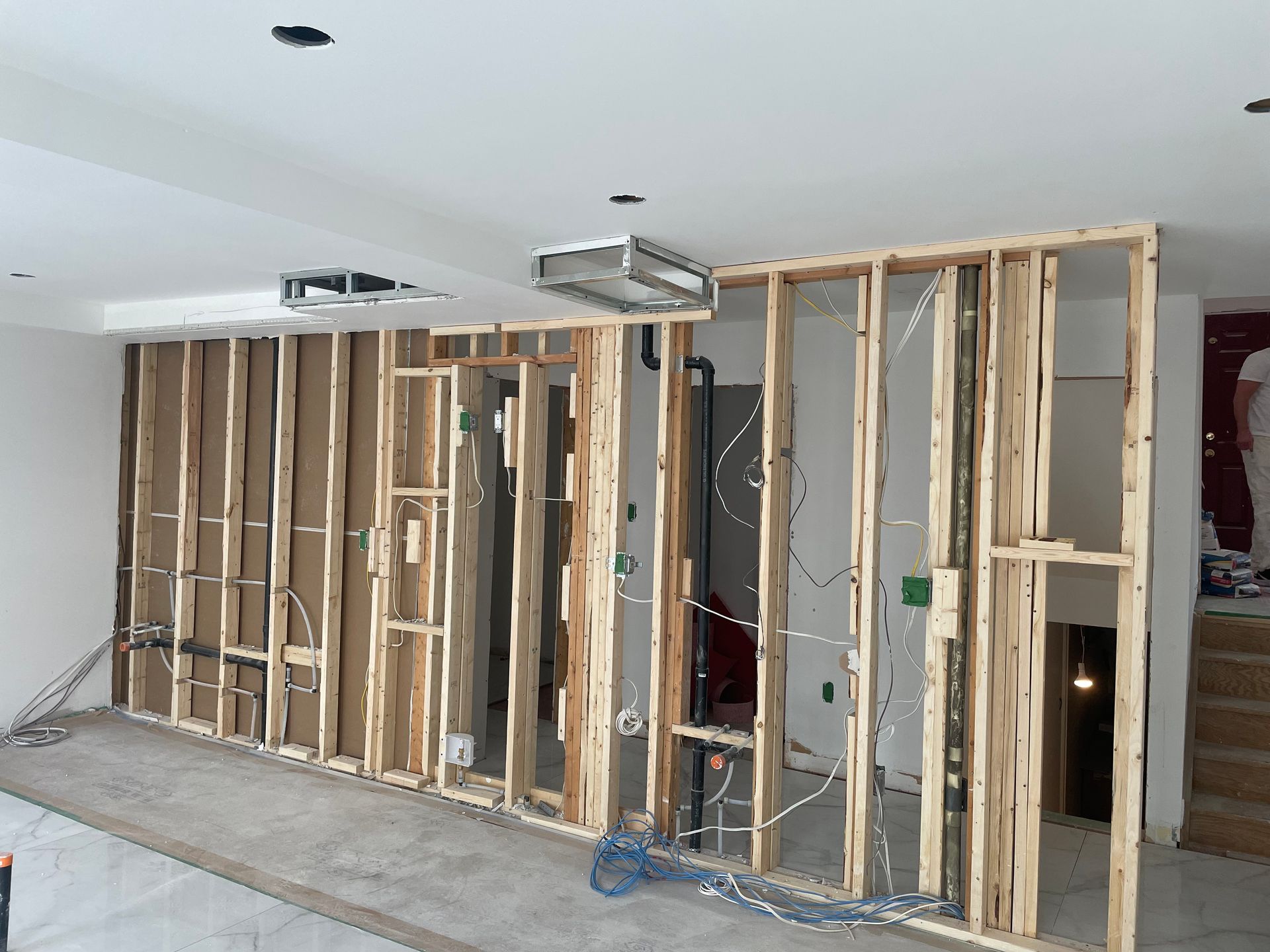 Interior framing of a wall in progress with electrical wiring, air vents and white walls.