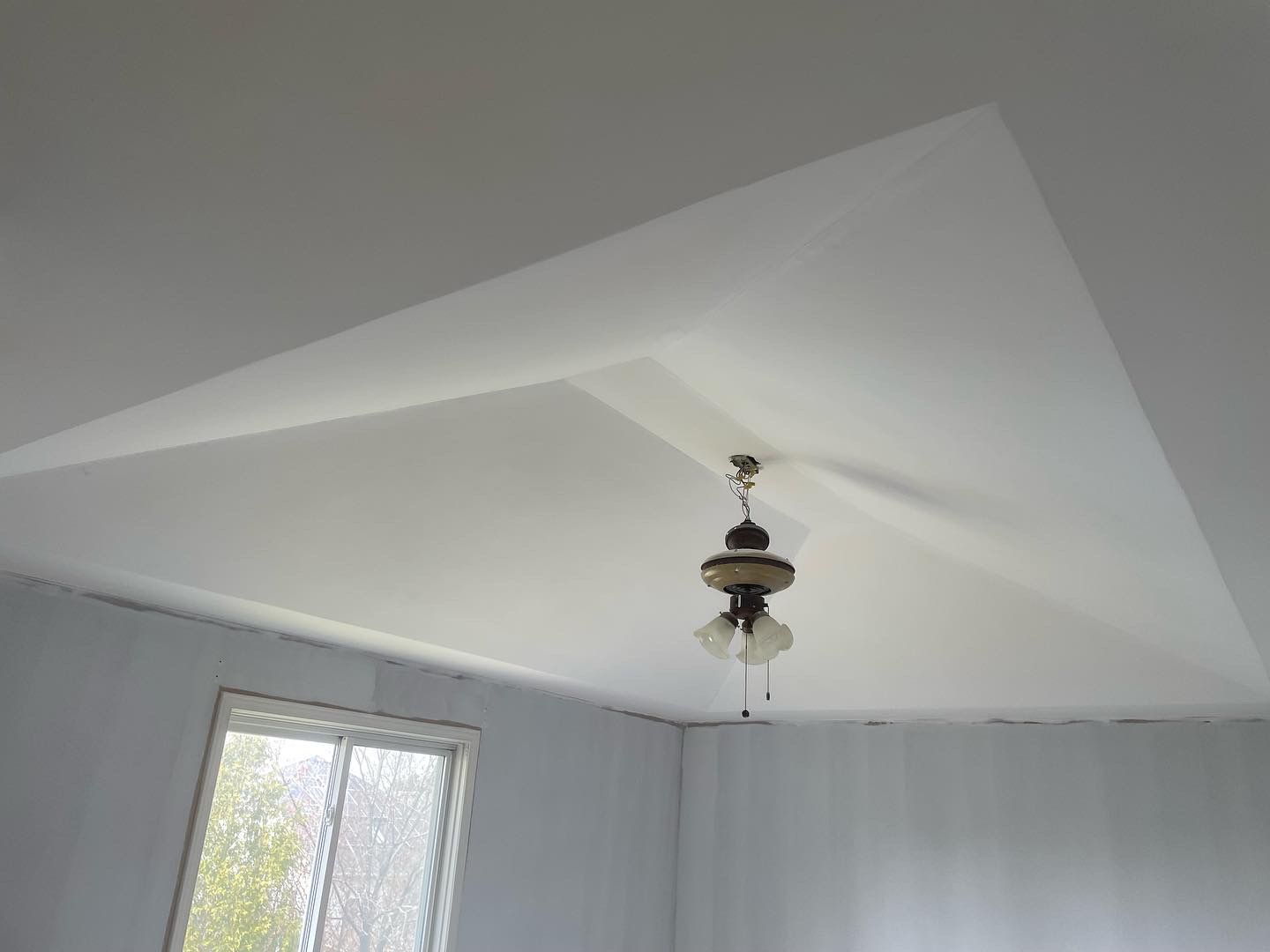 White vaulted ceiling with a hanging ceiling fan and light in a bright room