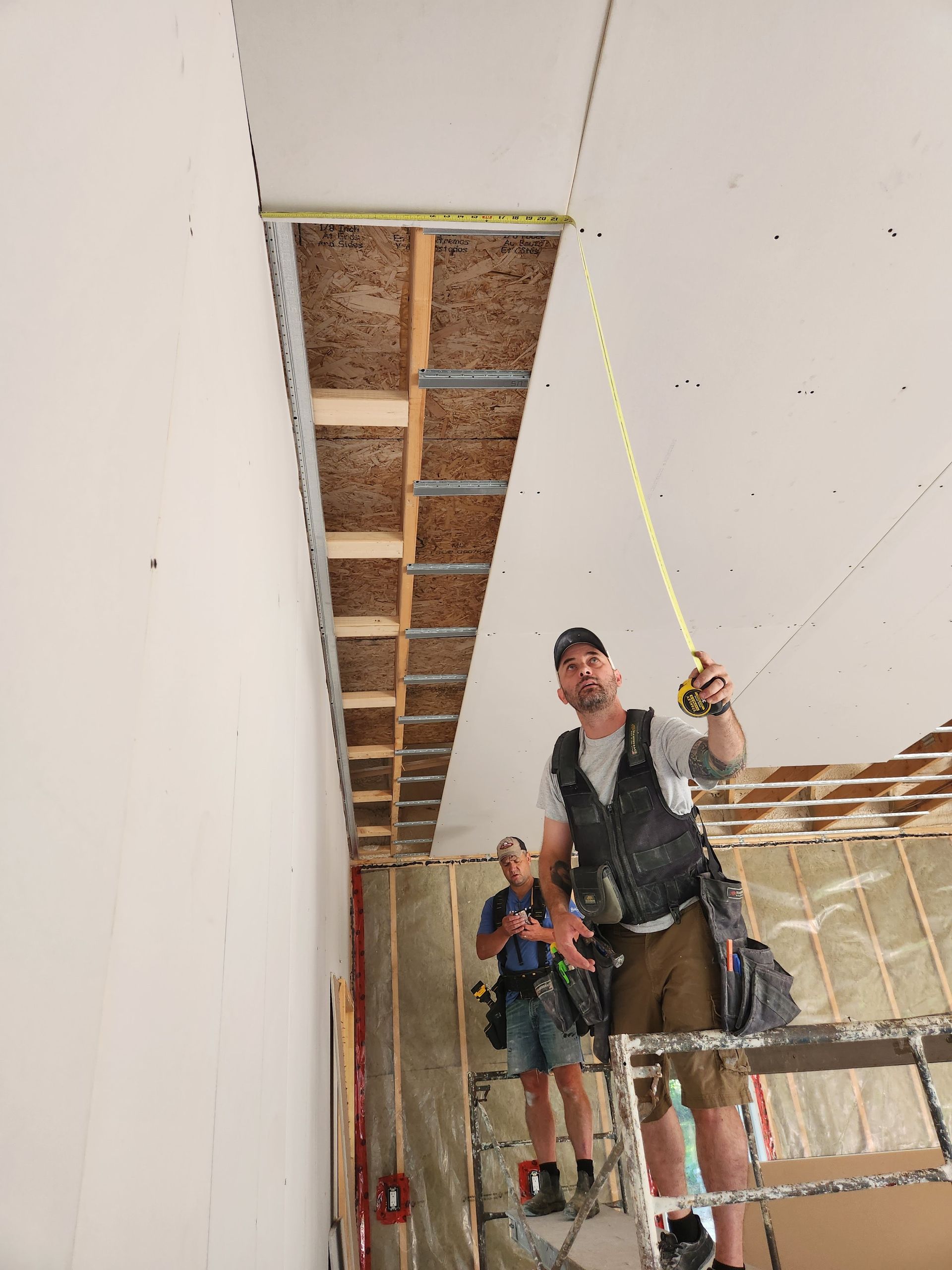 Two construction workers measure ceiling height with a tape measure on a construction site.
