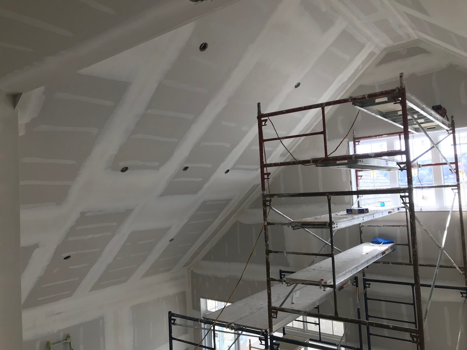 Scaffolding inside a white, unfinished room with vaulted ceiling panels and bright windows