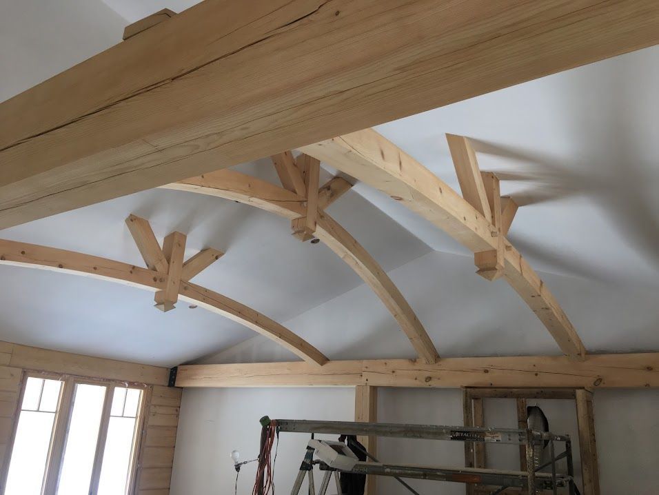 Wooden ceiling beams and trusses inside an unfinished room with scaffolding below.