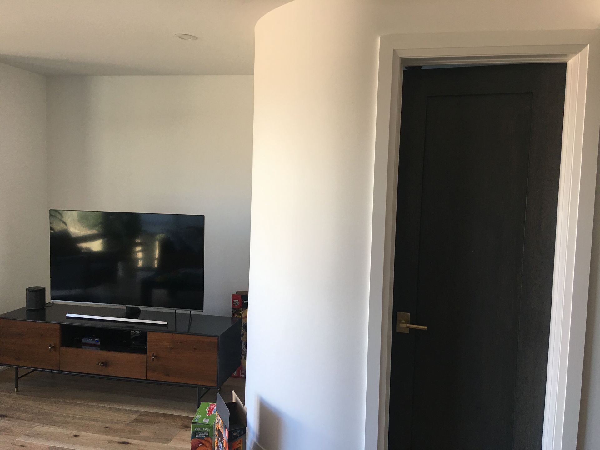 Living room with TV on a wooden console, black door, and white walls.