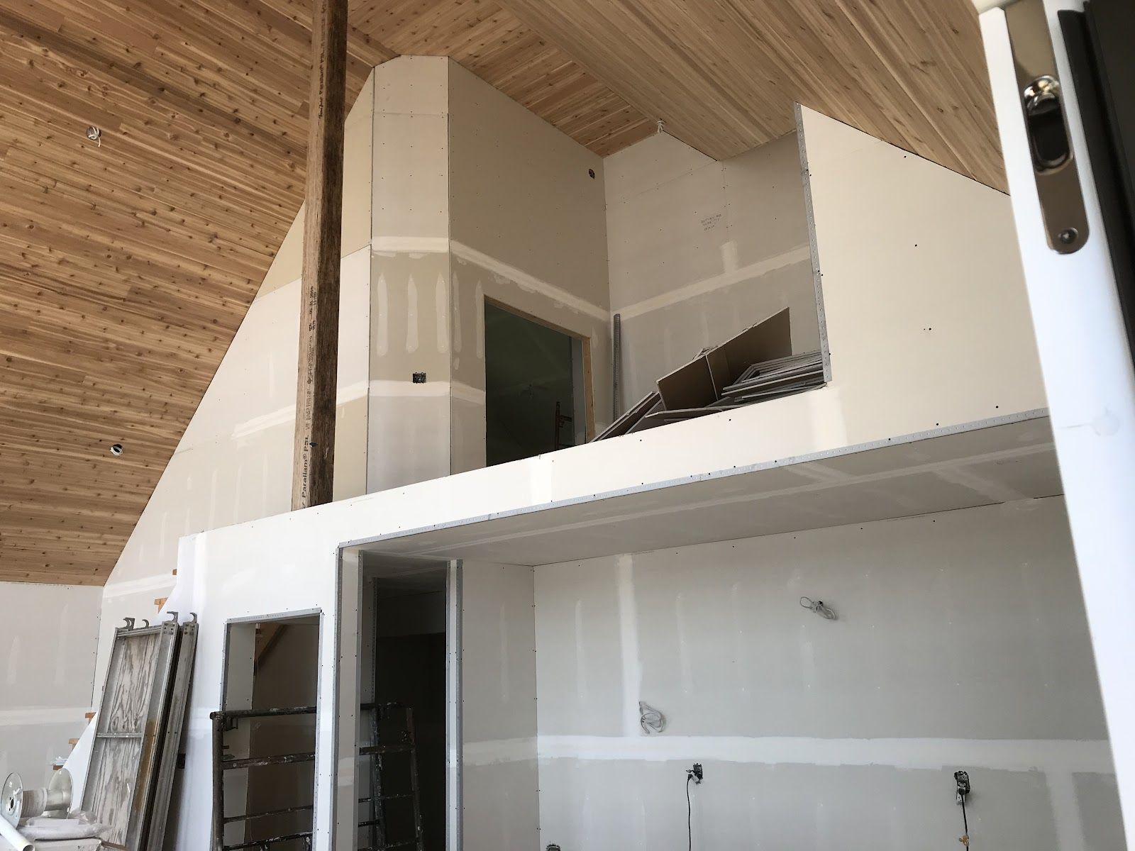 Modern loft interior with a white mezzanine, unfinished walls, and wood-paneled sloped ceiling