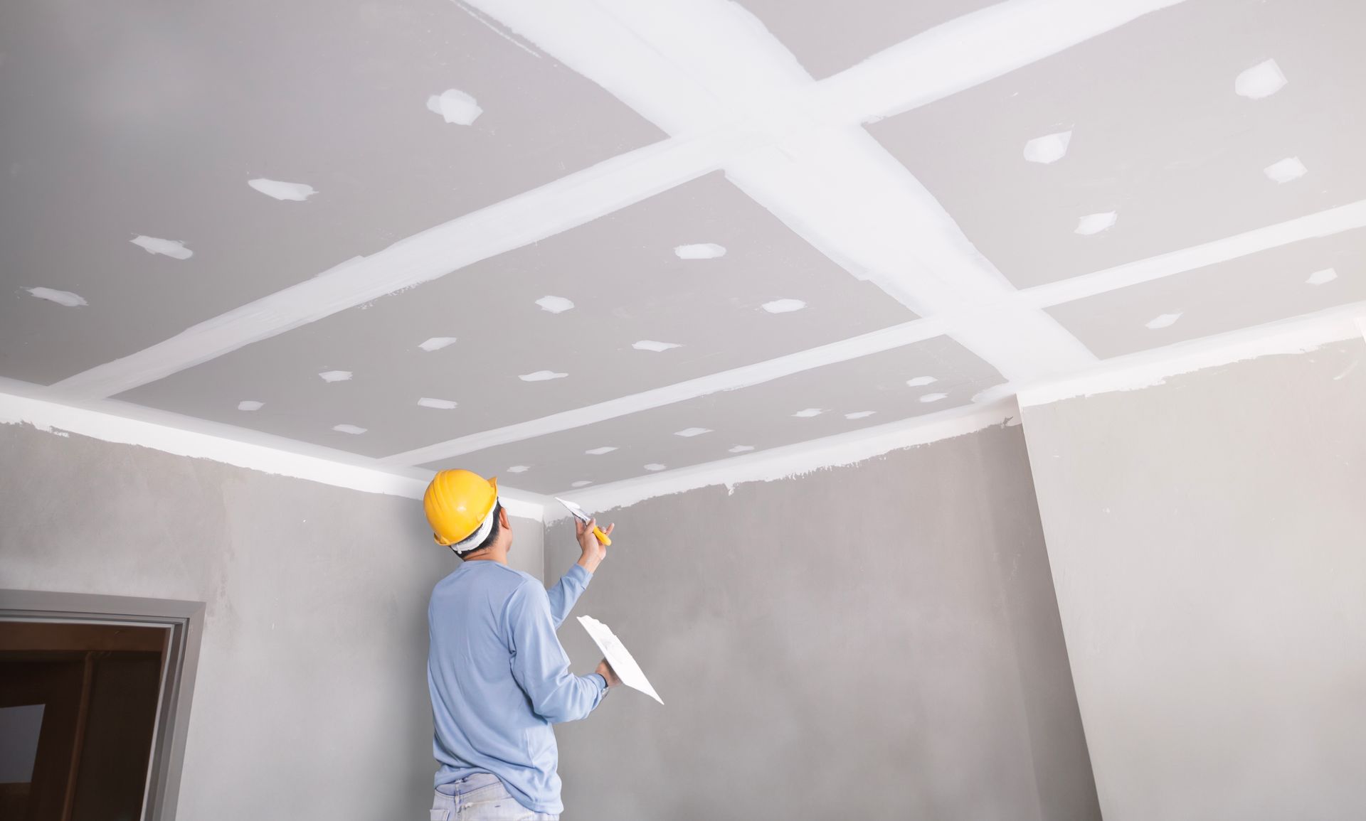 Person in hard hat applying drywall compound to a ceiling.