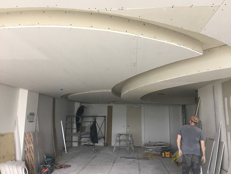 Construction workers install drywall on a curved ceiling in a room.