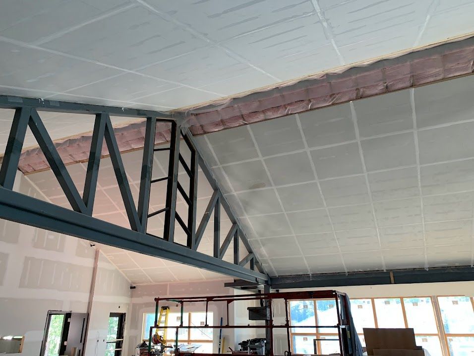 Interior under construction: Metal roof truss, drywall ceiling, pink insulation visible above.