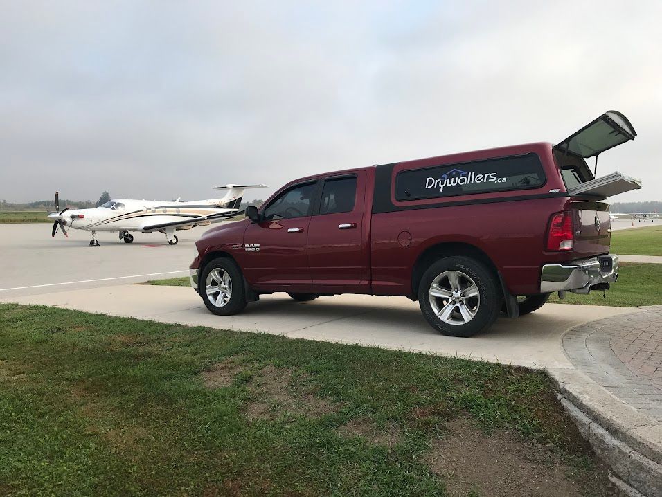 A red truck is parked on the side of the road next to a plane.