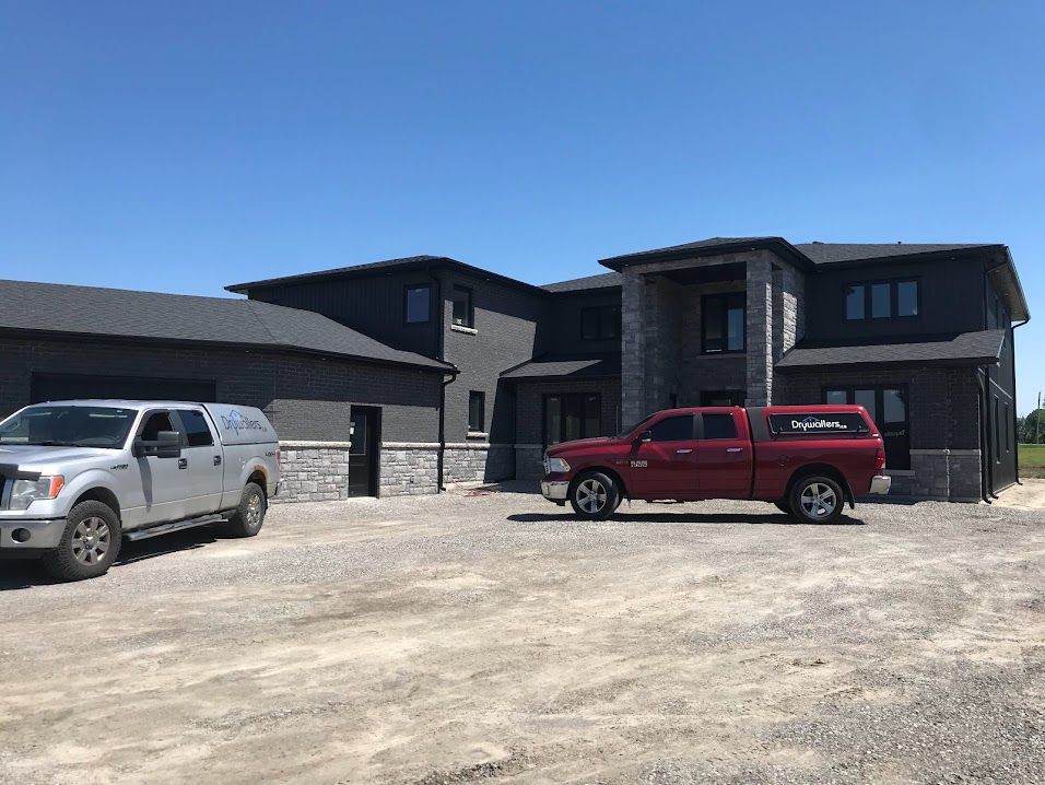 Two trucks parked in front of a modern two-story home with a stone and dark gray exterior.