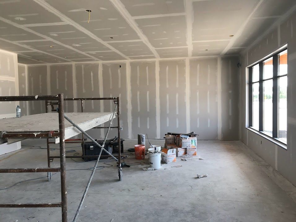 Interior room under construction, with drywall on walls and ceiling, scaffolding, and tools.