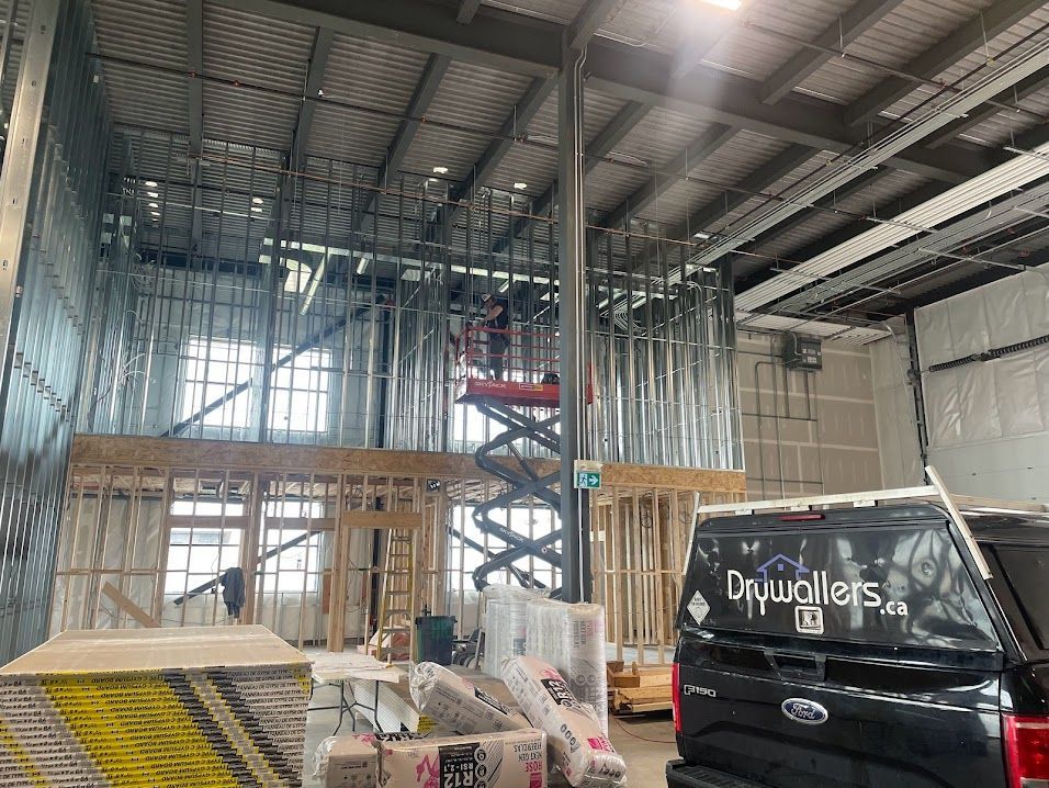 Interior construction site with metal and wood framing. A worker on a lift. A car with 