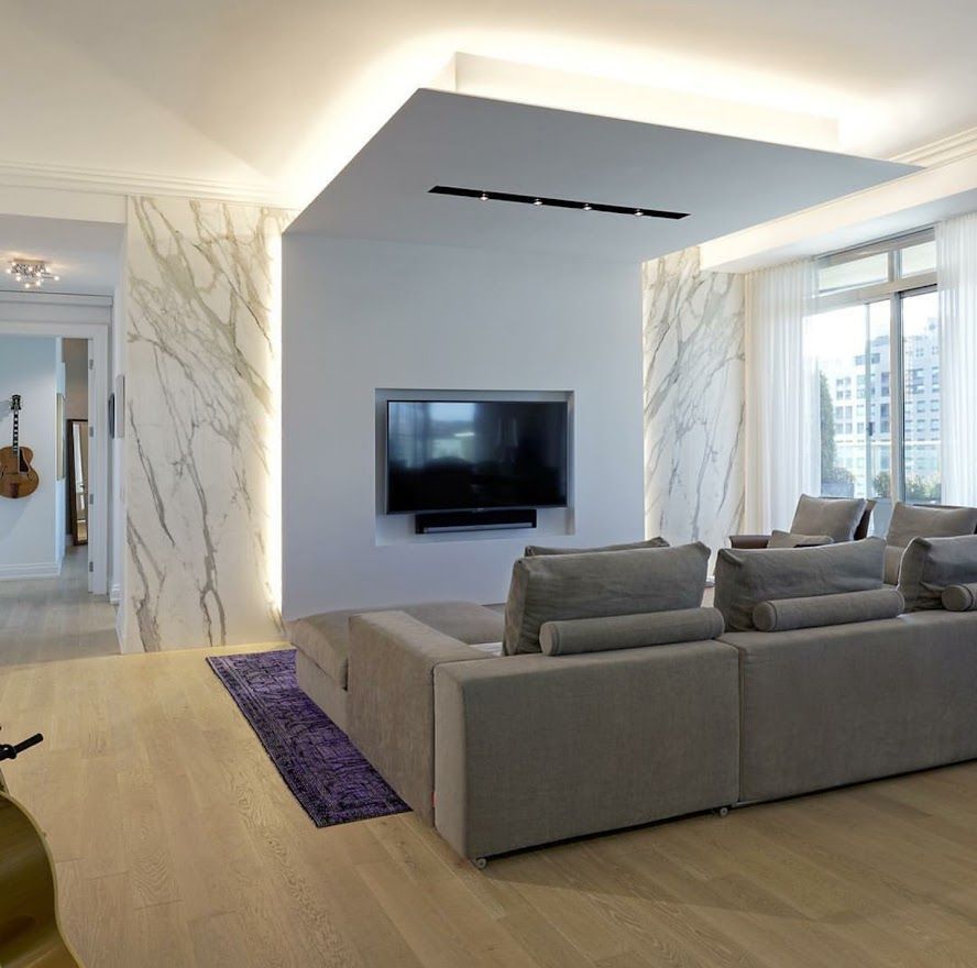 Modern living room with marble accents, large gray sectional, TV, and recessed lighting.