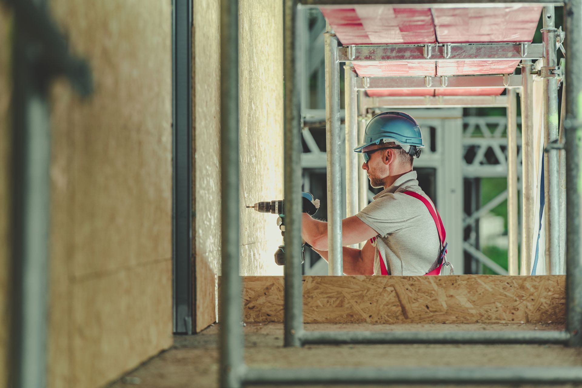 A construction worker is using a drill on a scaffolding.