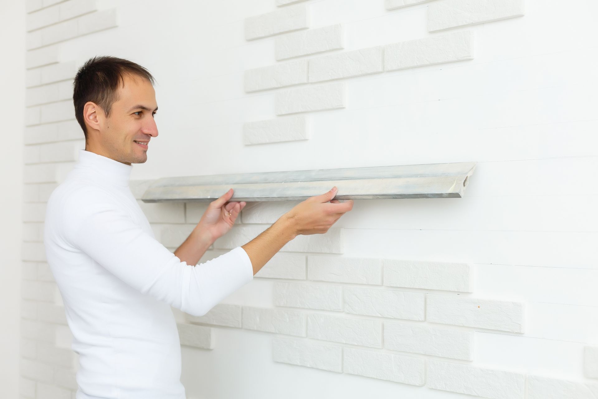 A man is installing a shelf on a white brick wall.