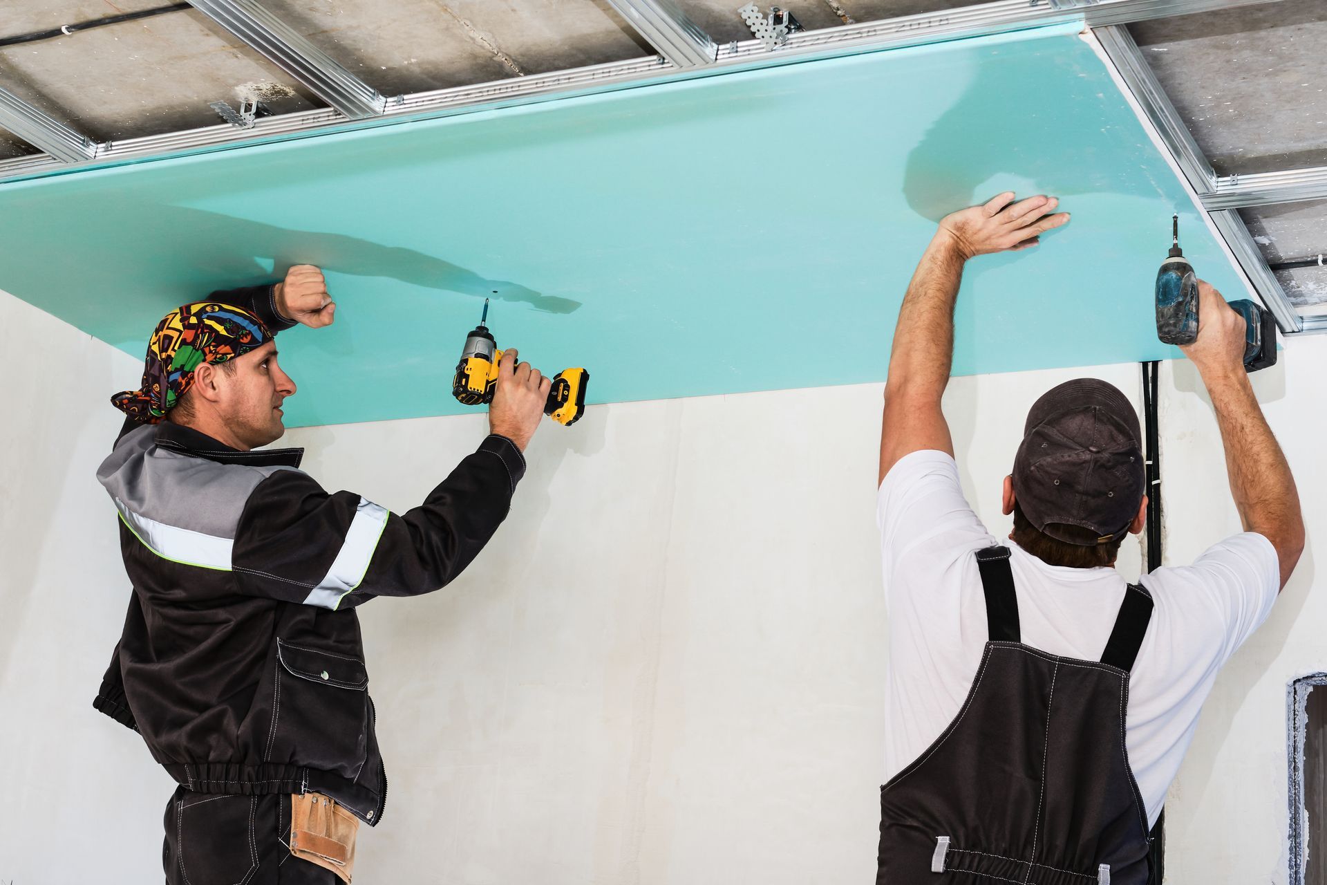 Two men are working on a ceiling with drills.