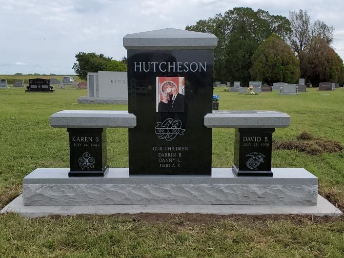 Black granite memorial headstone with photo, flanked by two smaller stones in a cemetery grass field.