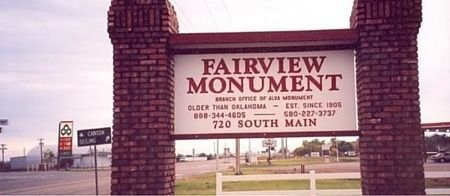 Fairview Monument sign between brick pillars at a roadside entrance, with a building and parking lot behind.