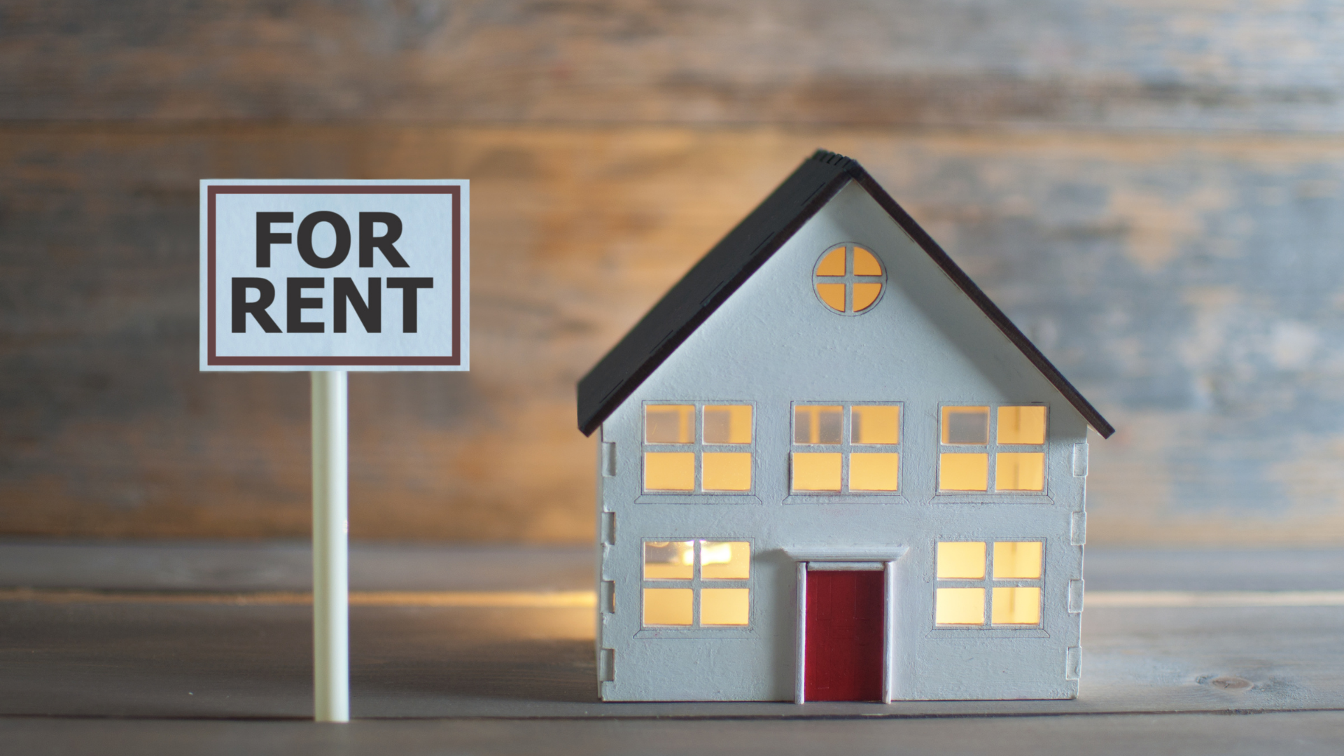 A model house is sitting next to a for rent sign.