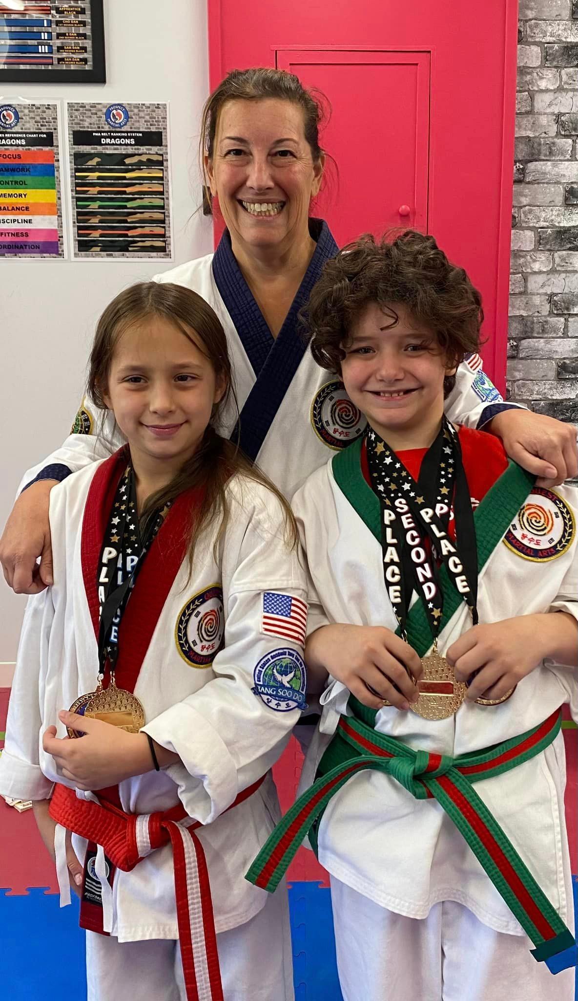 a woman is standing next to two children in karate uniforms holding medals .