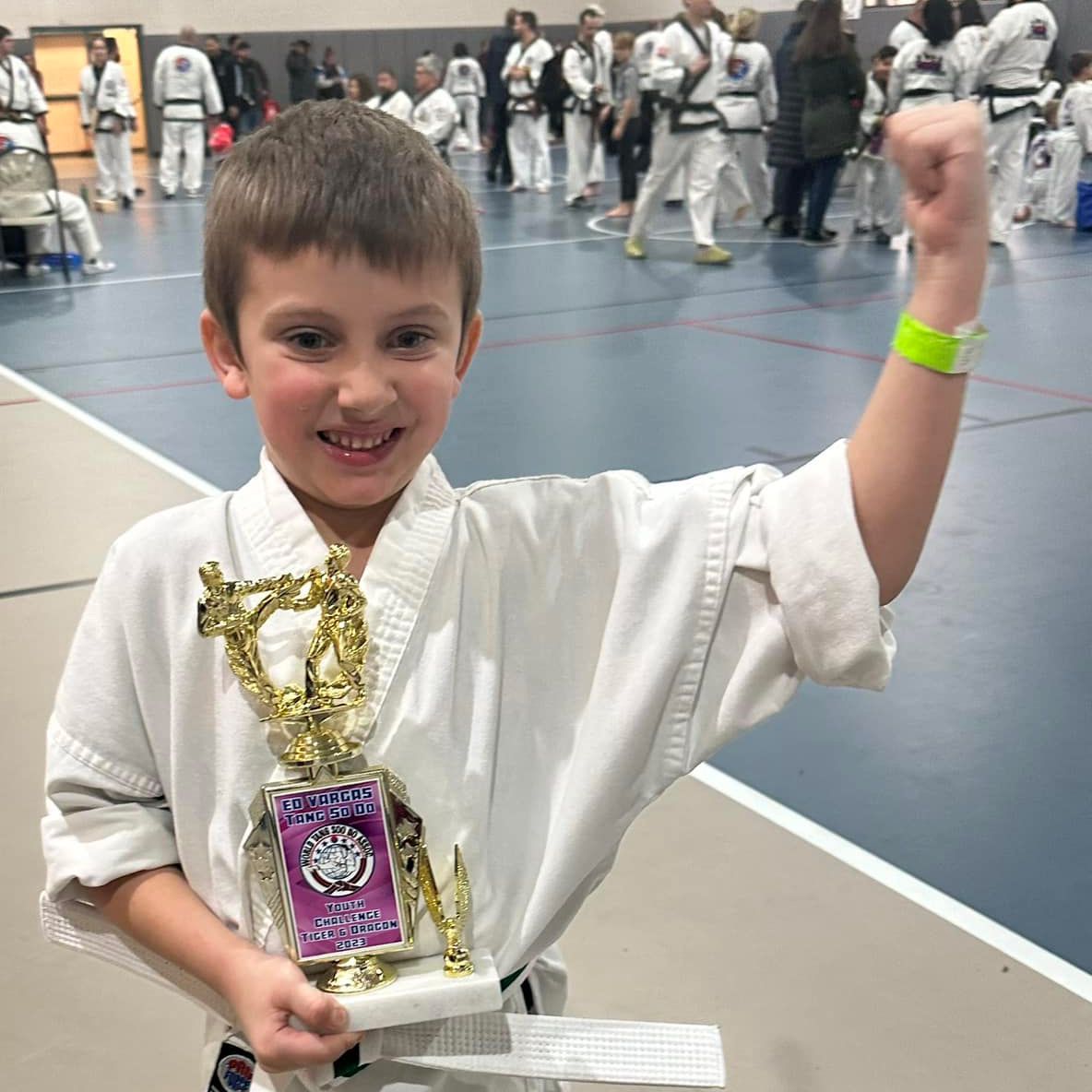 a young boy in a white karate uniform is holding a trophy .