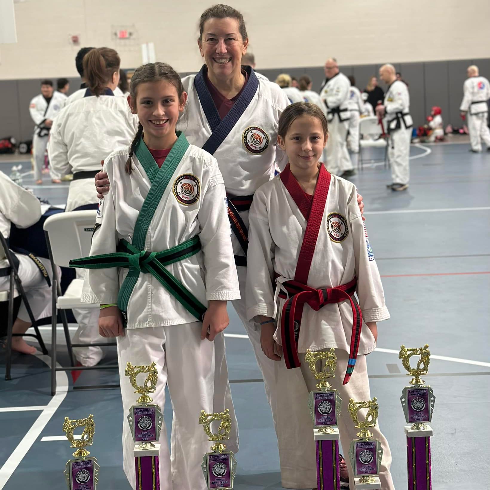 a woman and two young girls are standing next to trophies in a gym .