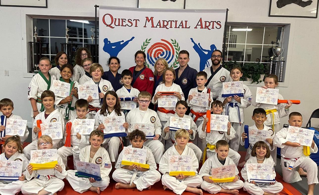 a group of children are posing for a picture in front of a quest martial arts sign .