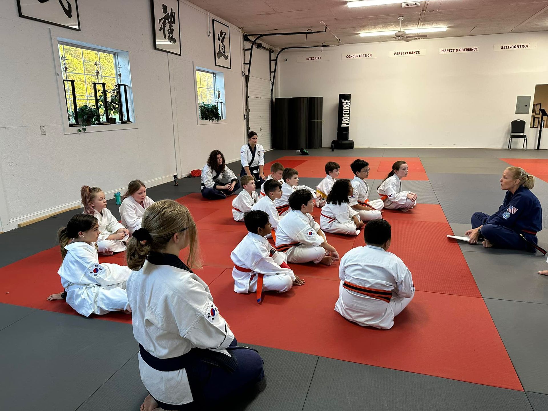 a group of children are sitting on the floor in a karate class .