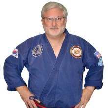 a man wearing a blue karate uniform and glasses is standing with his hands on his hips .