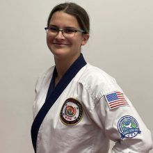 a woman wearing a white karate uniform and glasses is standing in front of a white wall .