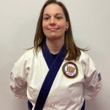 a woman is wearing a white karate uniform with a blue sash around her neck .