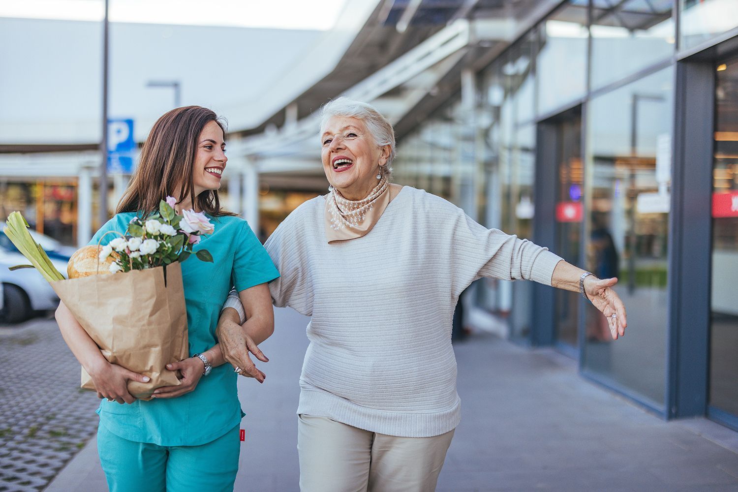 Two women walking outside a store, smiling and carrying flowers.