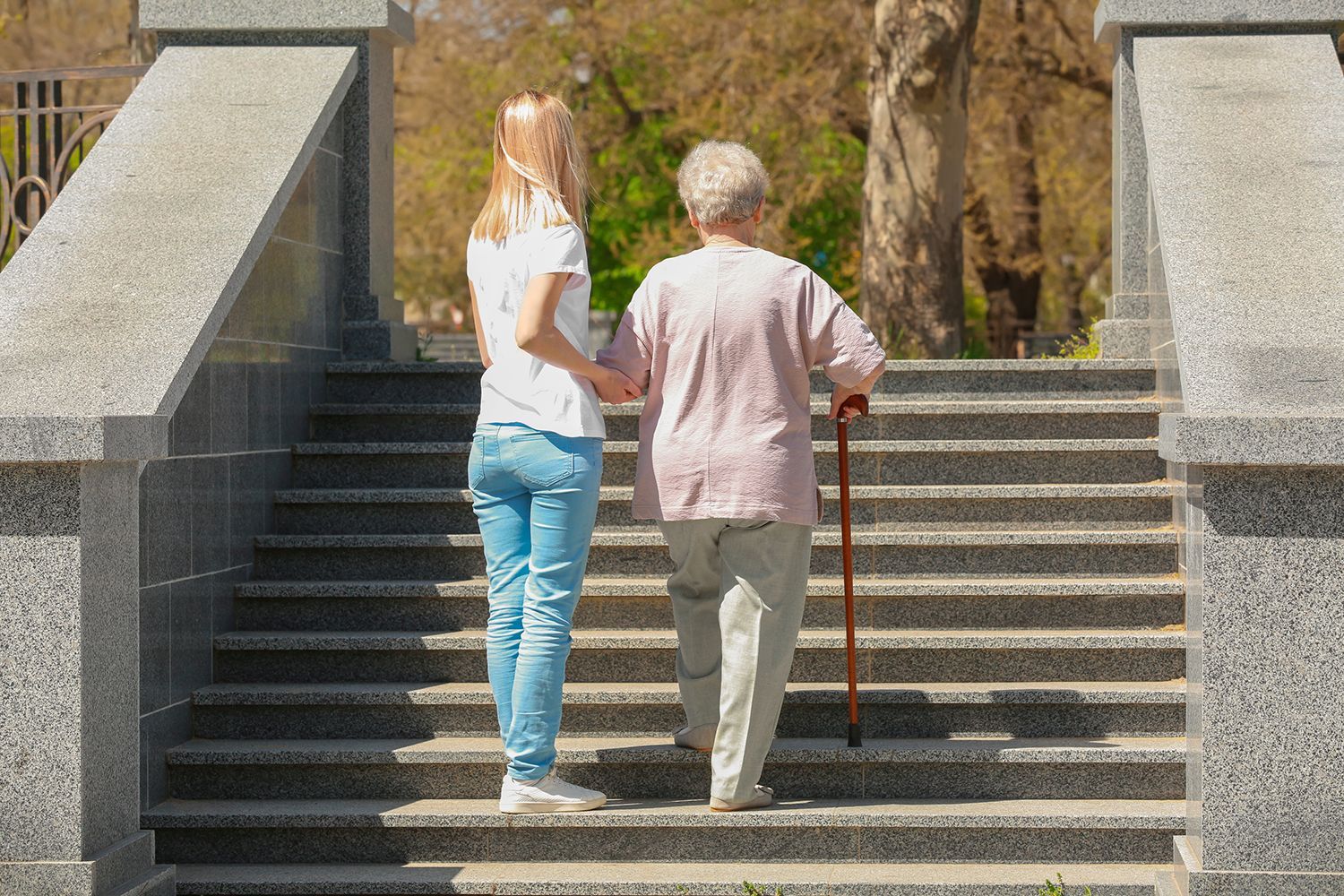 Two people ascending outdoor stone steps, one helping the other with a cane.