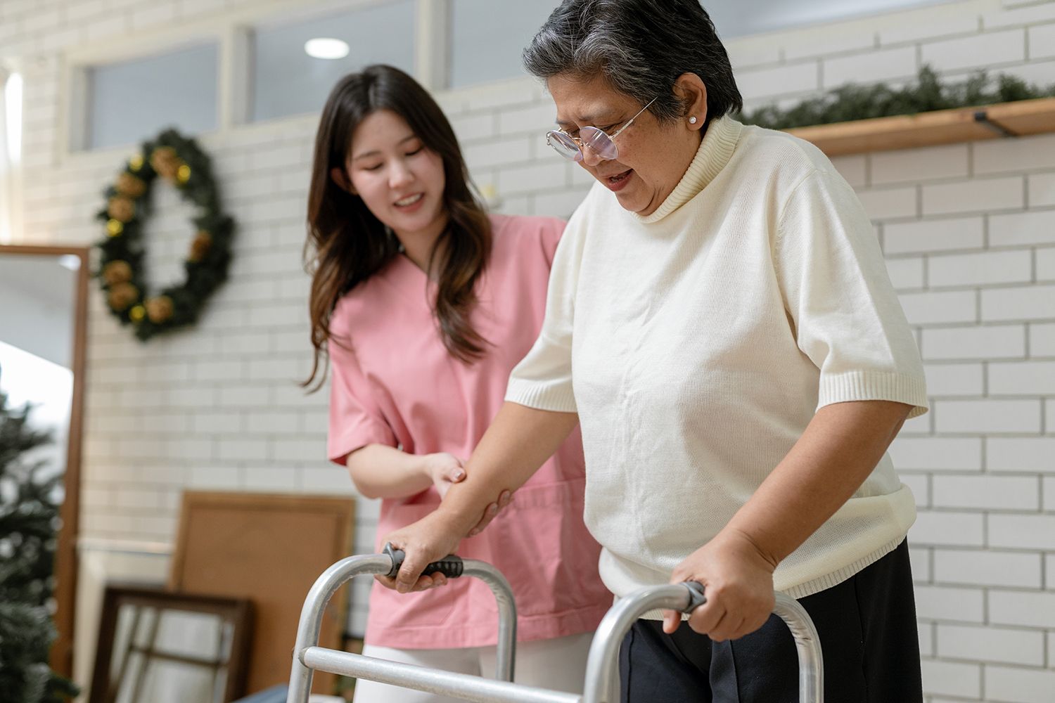 Two people smiling while using a walker indoors near a fireplace and holiday wreath. Two people smiling while using a walker indoors near a fireplace and holiday wreath.