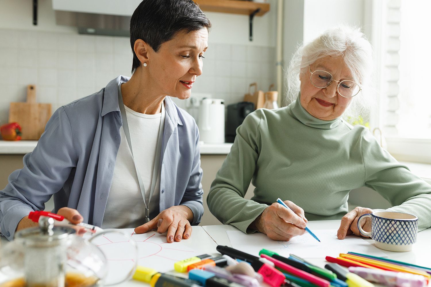 Two people drawing at a kitchen table with colorful markers and craft supplies Two people drawing at a kitchen table with colorful markers and craft supplies