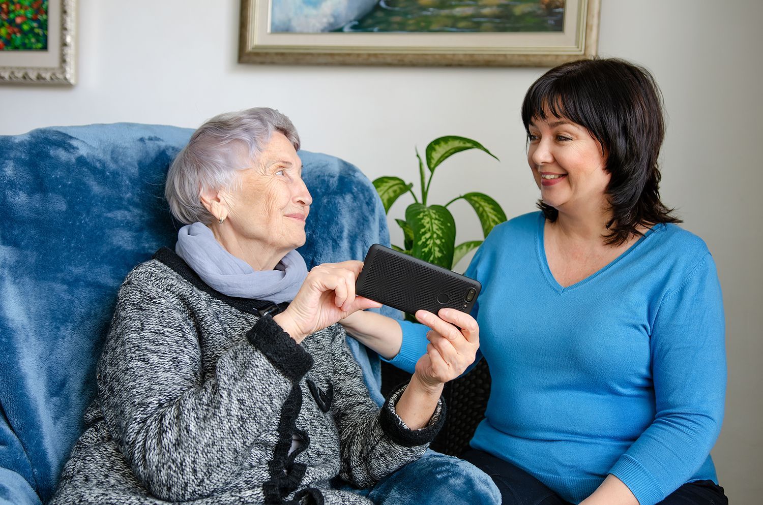 Two women sitting on a couch, smiling while looking at a smartphone