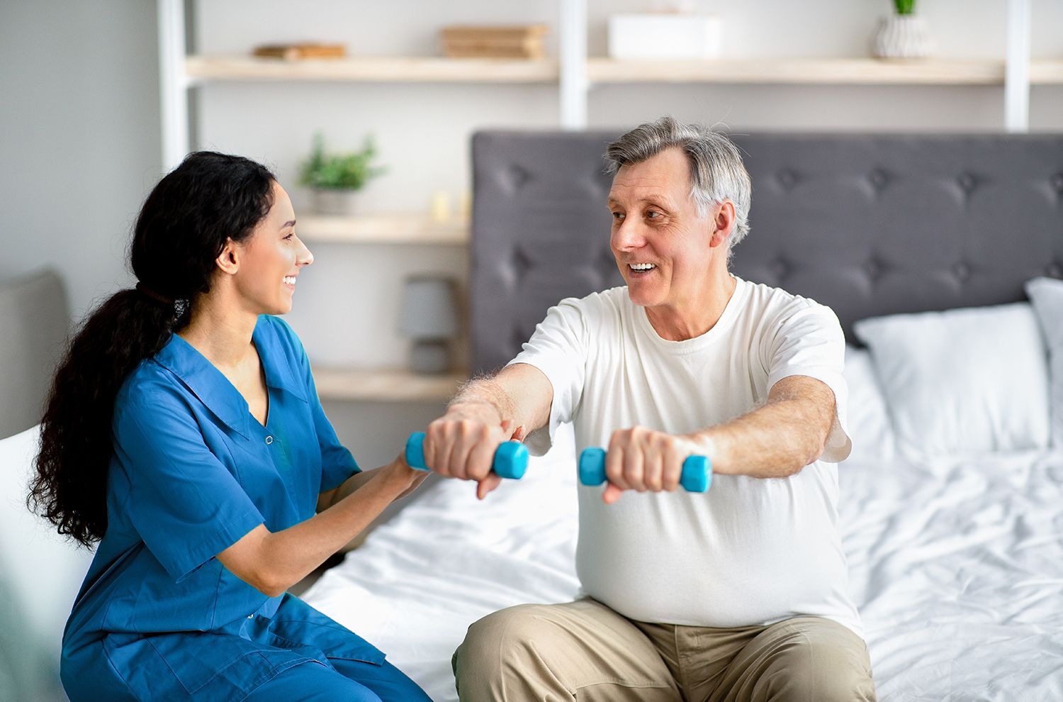 Two people exercising with dumbbells on a bed, smiling in a bright bedroom Two people exercising with dumbbells on a bed, smiling in a bright bedroom