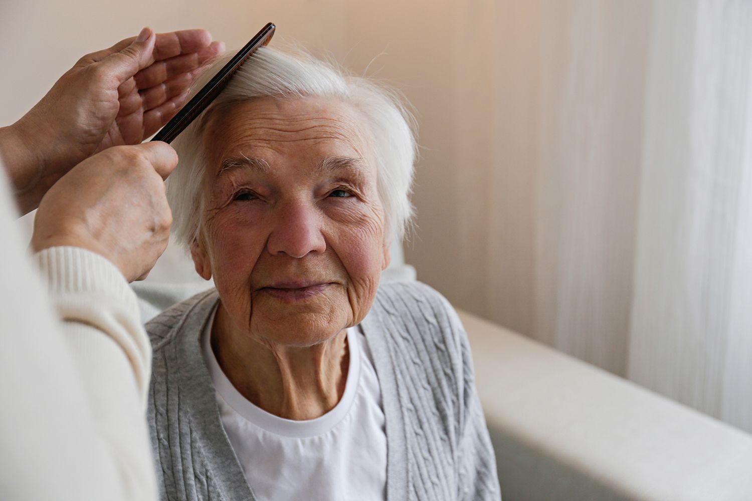 A person combs an elderly woman's hair in a softly lit room.
