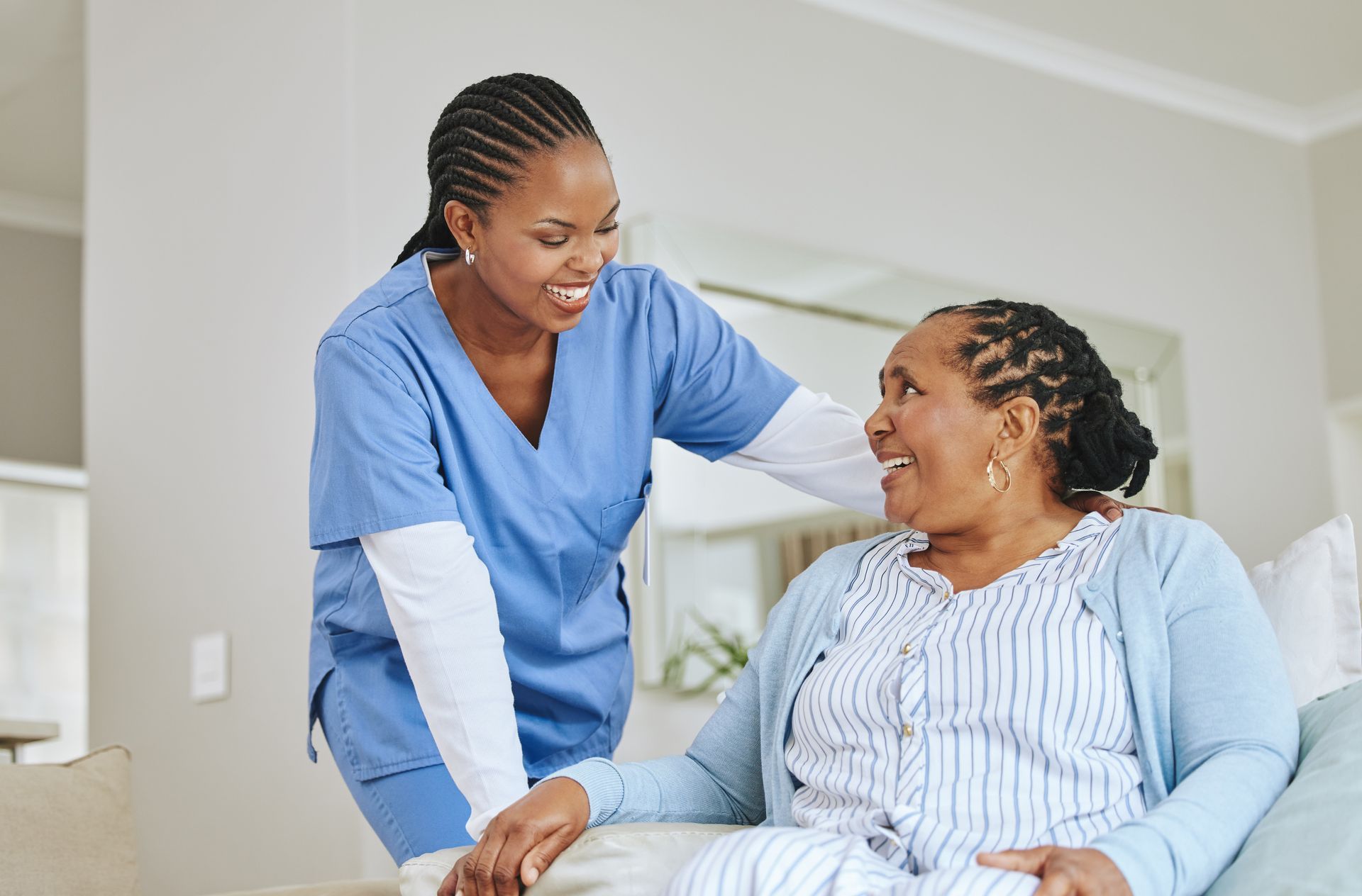 Nurse in blue scrubs smiling and speaking with a seated patient in a bright room