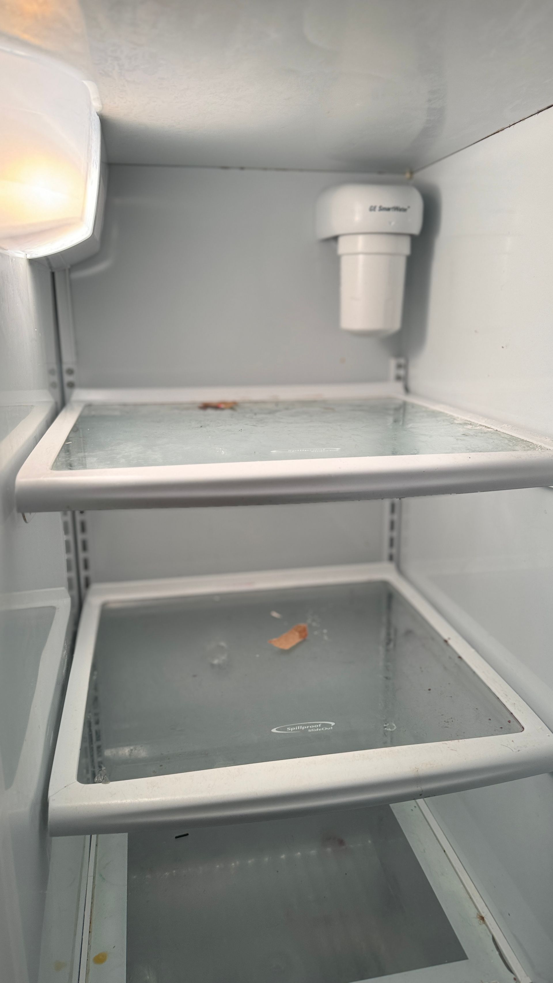 The inside of an empty refrigerator with two shelves and a water filter.