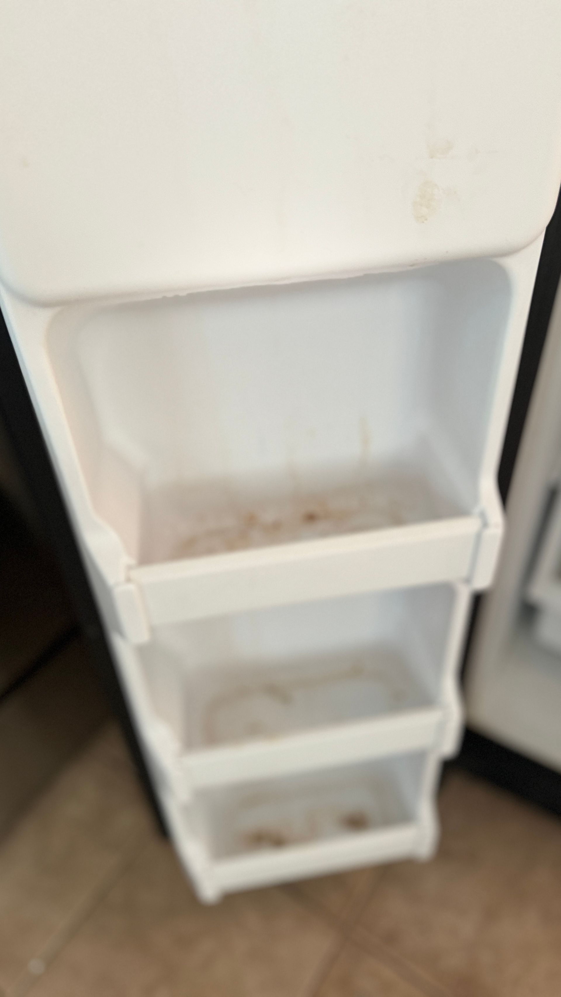 A white plastic shelf is sitting on a tiled floor next to a refrigerator.