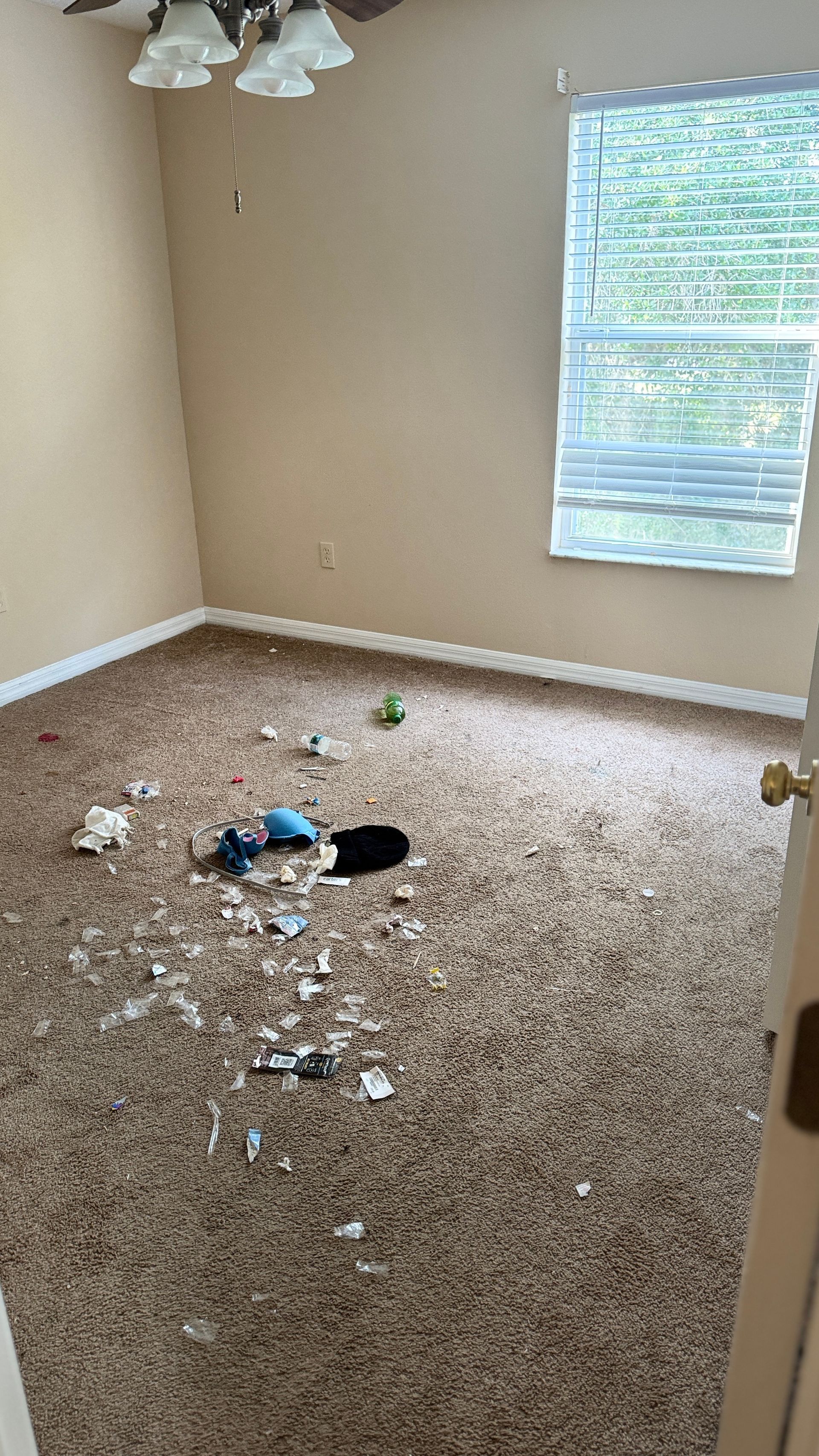 A room with a lot of trash on the floor and a window.