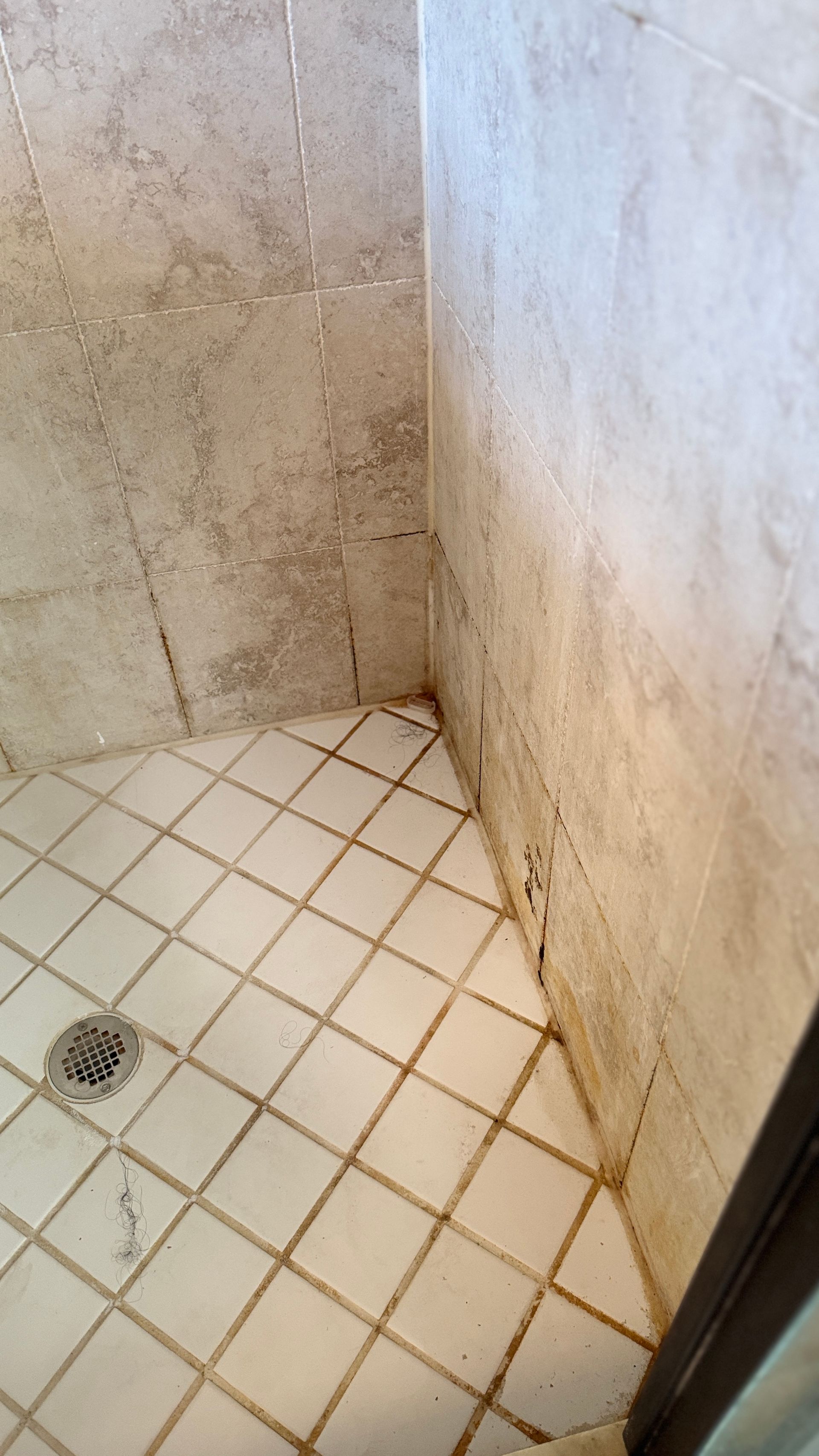 A shower stall with white tiles and a drain on the floor.