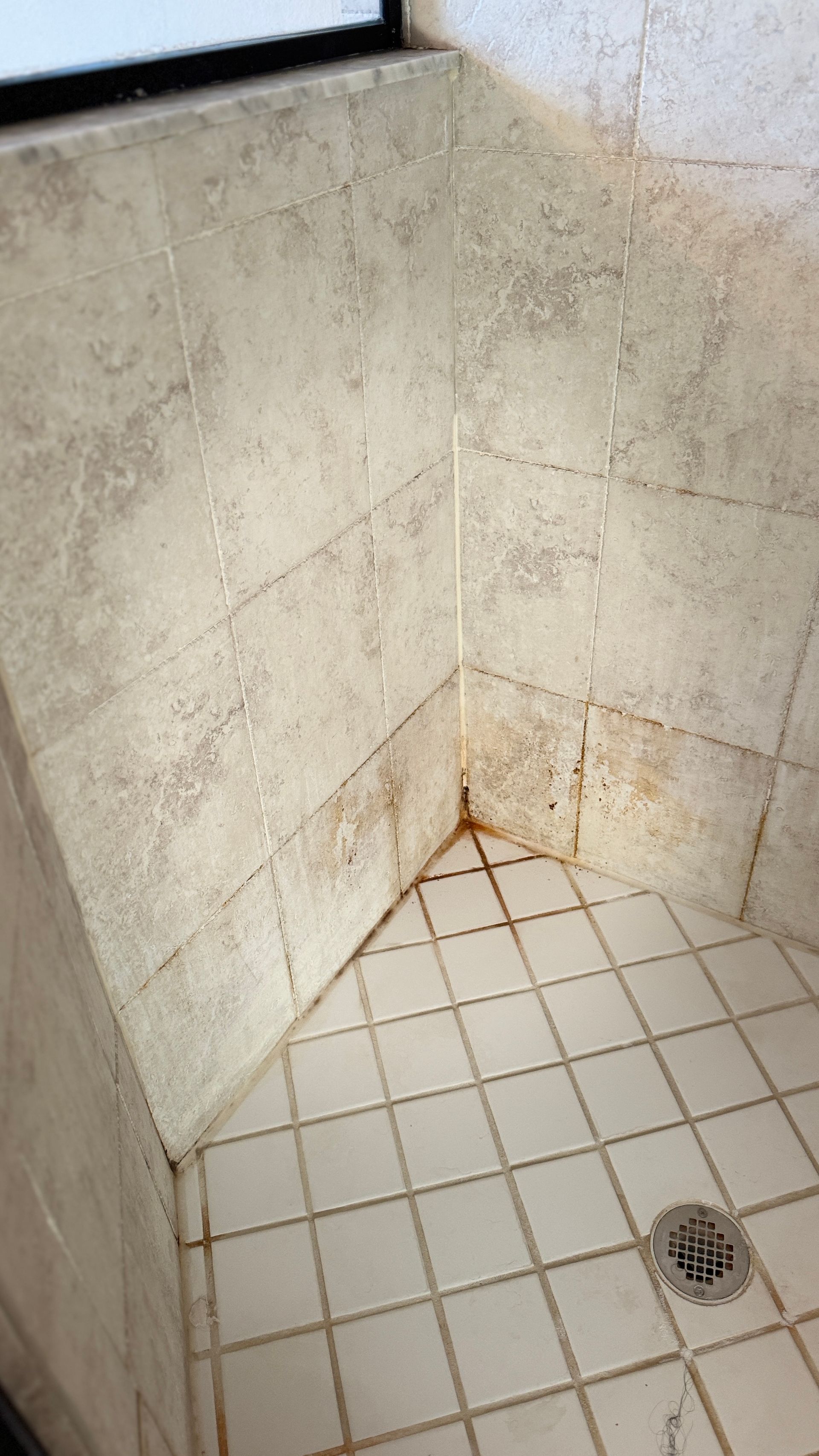 A dirty shower stall with white tiles and a drain.