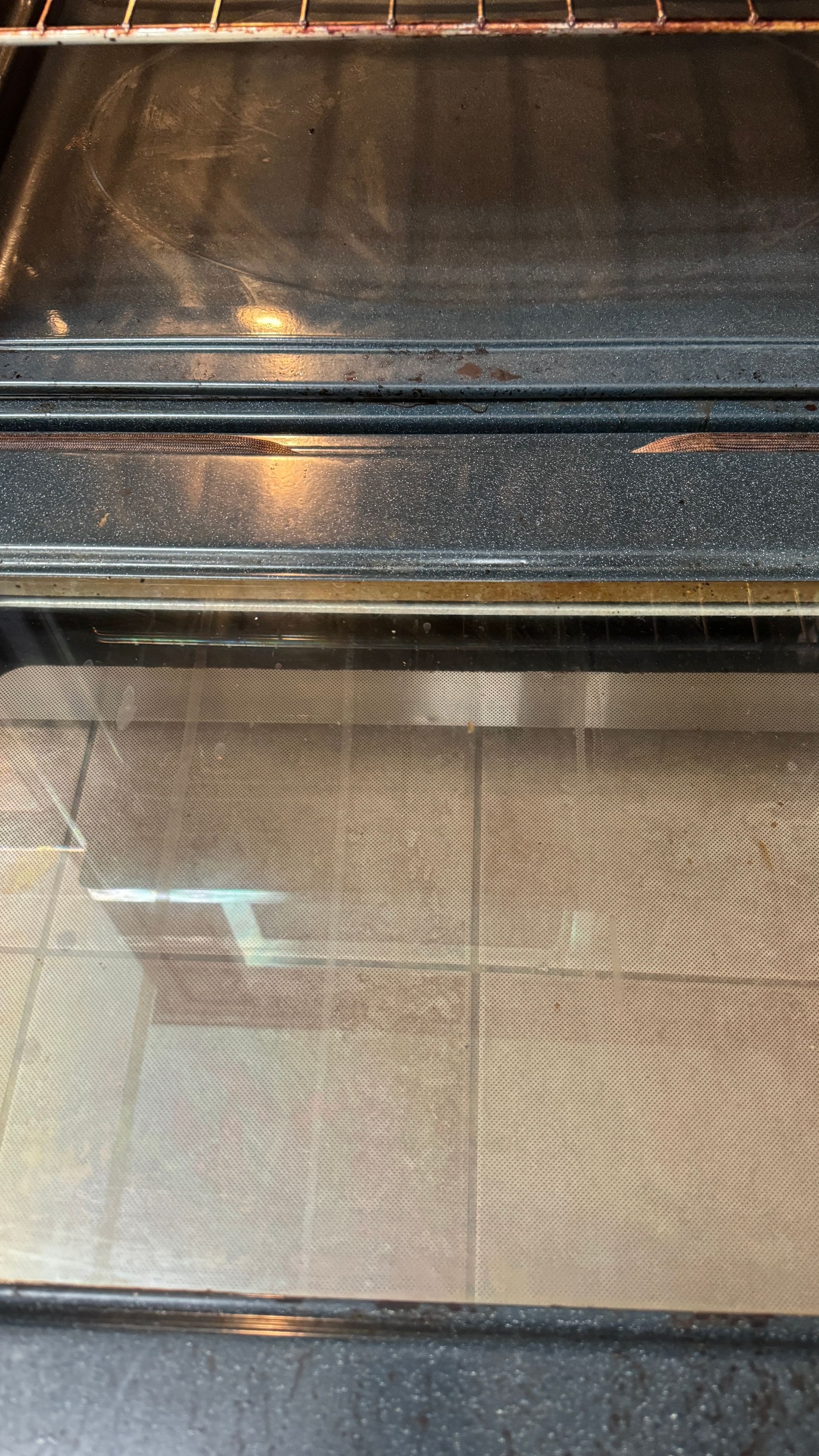 A dirty oven with a glass door is sitting on a tiled floor.