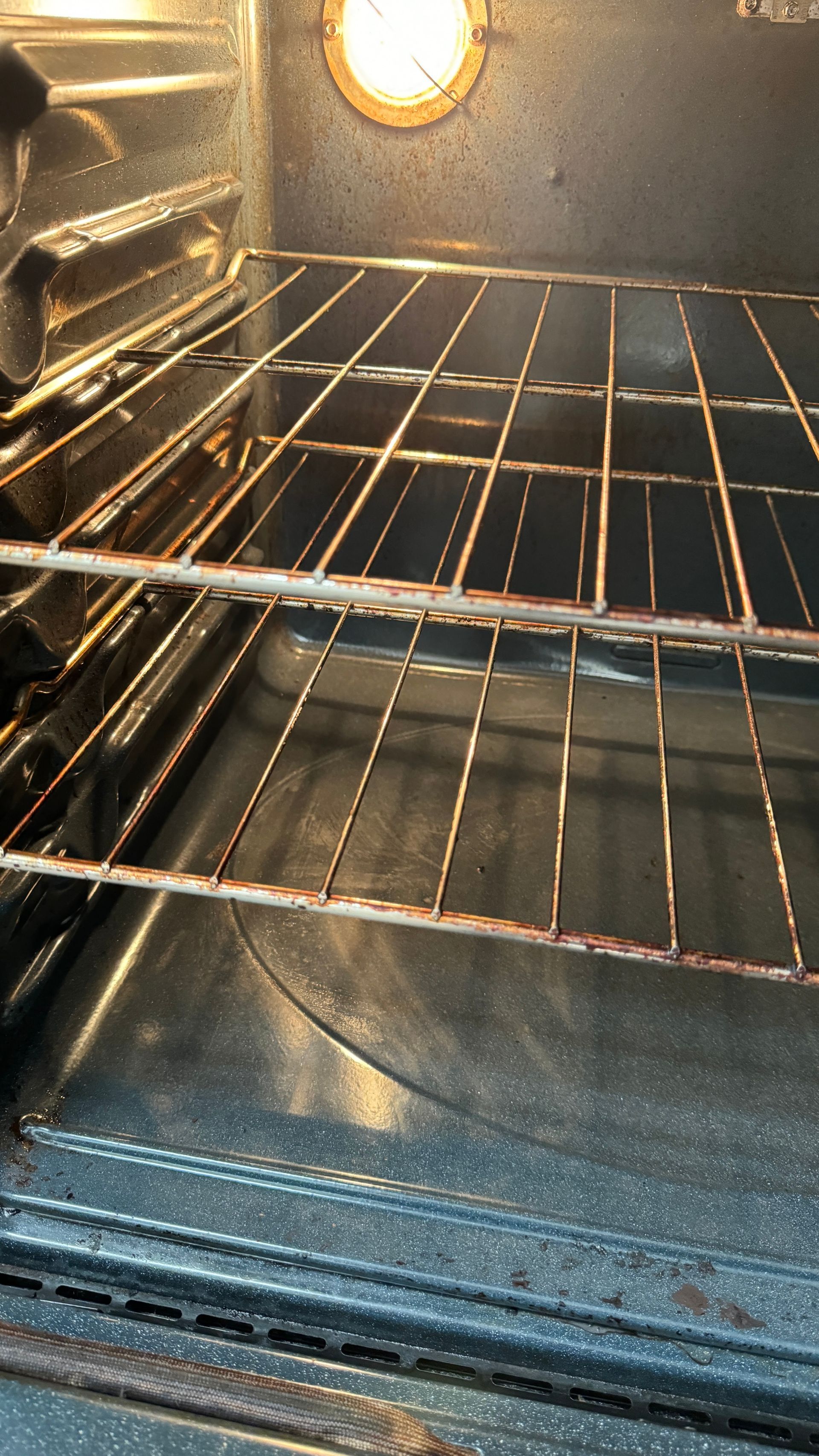 The inside of an oven with a wire rack and a light on.